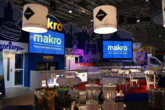 Stoisko targowe Makro CC na targach Eurogastro prezentuje kuchenne sprzęty i podświetlane szyldy, a całość rozświetlają duże lampy w przestronnej hali wystawowej. projekt i nadzór Tatjana Kobuszewska trksystem.com