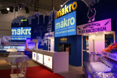 Stoisko targowe Makro CC na targach Eurogastro, z niebieskim oznakowaniem, ladą, sekcją Restauracja Pod Kaczorem i produktami spożywczymi wyeksponowanymi w regałach chłodniczych. projekt i nadzór Tatjana Kobuszewska trksystem.com