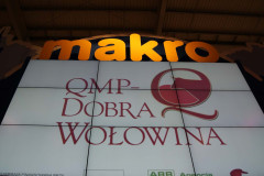 Duży znak makro góruje nad cyfrowym ekranem wyświetlającym logo QMP-Dobra Wołowina, z dodatkowymi małymi logo poniżej w stoisku targowym Makro CC podczas targów Eurogastro. projekt i nadzór Tatjana Kobuszewska trksystem.com