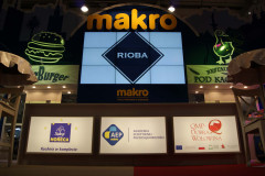 Duży podświetlany znak makro nad cyfrowymi i drukowanymi wyświetlaczami promującymi Rioba, Selg HORECA, AEP Makro i QMP Dobra Wołowina w stoisku targowym Makro CC podczas targów Eurogastro. projekt i nadzór Tatjana Kobuszewska trksystem.com