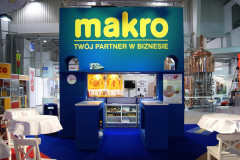 Niebiesko-żółte stoisko targowe Makro CC na targach Eurogastro, wyposażone w lady, ekspozytory, materiały promocyjne i otoczone innymi stoiskami wystawienniczymi i urządzeniami przemysłowymi. projekt i nadzór Tatjana Kobuszewska trksystem.com
