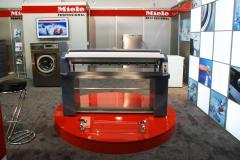 Stoisko Miele. Podest dla prasowalnicy. Czerwony błyszczący podest i szykowna szaroniebieska prasowalnica.  Szara wykładzina i dużo światła doskonale podkreślały elegancję profesjonalnych maszyn. By TRK System i Mateusz Stryjecki