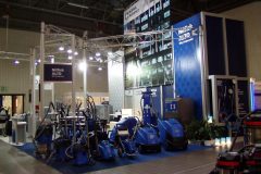 Stoisko targowe prezentuje różne niebieskie maszyny czyszczące i urządzenia odkurzające Nilfisk ALTO, z banerami, oświetleniem i informacjami o produktach na ścianach w przestronnej, krytej hali wystawowej. projekt i nadzór Tatjana Kobuszewska trksystem.com