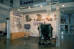 Stoisko wystawiennicze Nilfisk Advance obejmuje pojazd do czyszczenia ulic, banery promocyjne ze zdjęciami produktów, ekran telewizyjny, krzesła i stół na targach wewnętrznych. projekt i nadzór Tatjana Kobuszewska trksystem.com