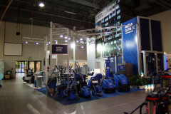 Kryte stoisko wystawowe prezentujące różne niebieskie maszyny i urządzenia do czyszczenia przemysłowego, z banerami i wyświetlaczami informacyjnymi w tle. projekt i nadzór Tatjana Kobuszewska trksystem.com