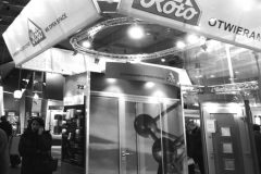 Czarno-białe zdjęcie przedstawia podwójne stoisko marki „Roto” z dużymi szyldami reklamowymi, wyświetlaczem ze zdjęciem satelitarnym i kilkoma osobami spacerującymi w pobliżu okna dachowego w hali wystawowej. projekt i nadzór Tatjana Kobuszewska trksystem.com