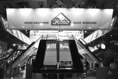 Czarno-białe zdjęcie podwójnego stoiska Roto, eksponującego okna dachowe. Na stoisku znajdują się duże eksponaty okna dachowe oraz napisy w języku polskim i angielskim z napisami „OKNA DACHOWE” i „ROOF WINDOWS” pod logo Roto. projekt i nadzór Tatjana Kobuszewska trksystem.com