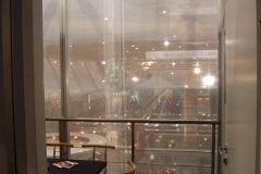 Niewielka, przeszklona sala konferencyjna z czarnym stołem, czerwonymi krzesłami i widokiem na jasno oświetloną przestrzeń wystawową z podwójnym stoiskiem przez duże okna. projekt i nadzór Tatjana Kobuszewska trksystem.com