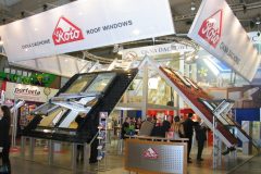 Stoisko wystawowe firmy „roto Roof Windows” na targach Budma, na którym prezentowany był duży ekspozytor okien dachowych z czarnymi i czerwonymi gontami, recepcja, banery oraz ludzie wchodzący w interakcje w dobrze oświetlonej przestrzeni wewnętrznej. projekt i nadzór Tatjana Kobuszewska trksystem.com