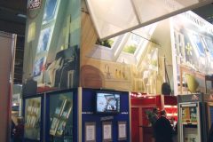 Stoisko targowe na targach Budma z dużymi panelami zadrukowanymi, prezentującymi okna dachowe Roto i wnętrza pokoi, ekranem telewizyjnym, oprawnymi certyfikatami i ludźmi gromadzącymi się wokół ekspozycji w krytej hali wystawowej. projekt i nadzór Tatjana Kobuszewska trksystem.com