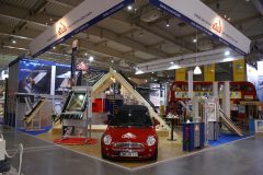 Stoisko targowe prezentuje czerwonego mini coopera, ekspozytor okien i modele dachowe pod dużym banerem „Roto”. Niebiesko-biała marka Roto okna dachowe wyróżnia się w przestronnej hali wystawowej. projekt i nadzór Tatjana Kobuszewska trksystem.com