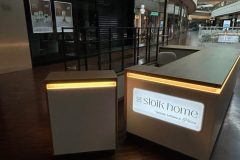 Nowoczesne wnętrze centrum handlowego z przyćmionym oświetleniem. Na pierwszym planie znajduje się recepcja ze świecącym napisem Sloik home, ponieważ kuchnie są włoskie. W tle widoczny jest zamknięty sklep Tchibo wraz z balustradami na górnym poziomie. projekt i nadzór Tatjana Kobuszewska trksystem.com