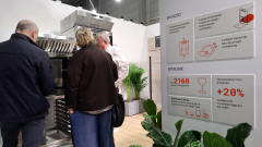 Trzy osoby przyglądają się dużemu piecowi przemysłowemu na stoisku wystawowym. Po prawej stronie wyświetlacz informacyjny w języku polskim podkreśla funkcje i statystyki pieca za pomocą ikon i tekstu. Zielone rośliny zdobią stoisko, a otoczenie wygląda nowocześnie i profesjonalnie. projekt i nadzór Tatjana Kobuszewska trksystem.com