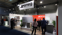 Grupa ludzi stoi i rozmawia na stoisku Smeg Professional  Stoisko ma nowoczesny, czysty design z roślinami i ekspozycją produktów. projekt i nadzór Tatjana Kobuszewska trksystem.com