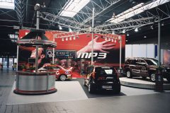 Muzyczne stoisko JVC zawiera czarny samochód z oznakowaniem JVC Mobile, czerwony SUV, ladę wystawową i duże tło z grafiką MP3 i wyciągniętą ręką. projekt i nadzór Tatjana Kobuszewska trksystem.com