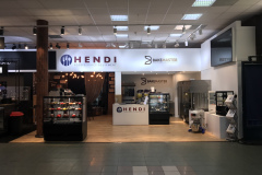 Dobrze oświetlony salon wystawowy prezentuje sprzęt gastronomiczny Hendi i Bakemaster. Szklane gabloty prezentują produkty, a lady z markowymi znakami są widoczne. Przestrzeń ma drewnianą podłogę, nowoczesne oświetlenie i różne urządzenia na wystawie. projekt i nadzór Tatjana Kobuszewska trksystem.com