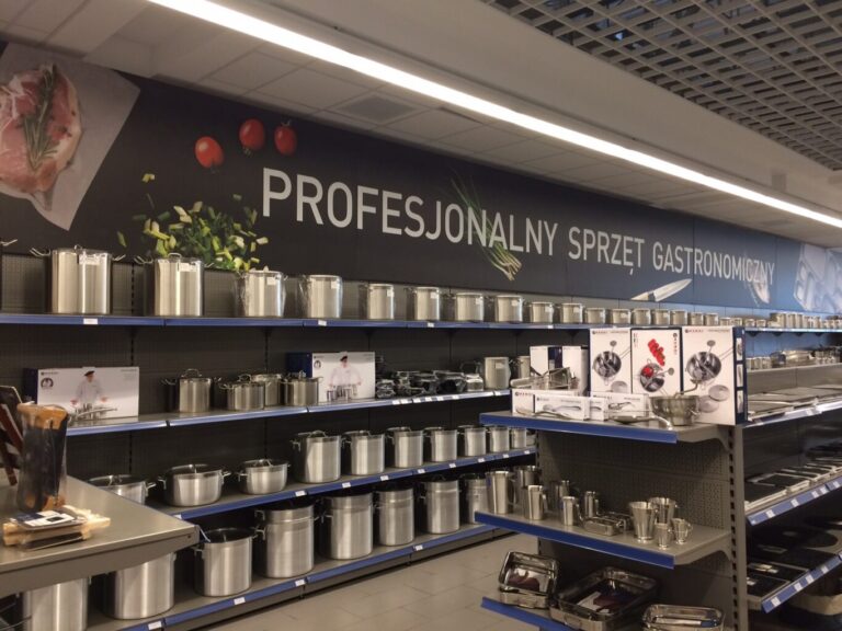 W alejce sklepowej na półkach stoją rzędy błyszczących naczyń ze stali nierdzewnej. Powyżej widnieje napis w języku polskim „Profesjonalny sprzęt gastronomiczny”, a na wyświetlaczu widnieje projekt i wymiana Tatjana Kobuszewska, trksystem.com. projekt i nadzór Tatjana Kobuszewska trksystem.com
