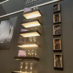 Ekspozytor ścienny dla marki Fine Dine, zainspirowany przez Kongres szefów kuchni FineDine, zawierający podświetlane półki z kieliszkami do wina i szklankami, oprawione w czarne ramy pudełka z zestawami sztućców, a wszystko to na tle ciemnej ściany z logo i obrazami nakrycia stołu powyżej. projekt i nadzór Tatjana Kobuszewska trksystem.com