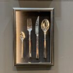 Na szarej ścianie zamontowano oprawioną w ramę ekspozycję srebrnych sztućców. Wewnątrz ramy naczynia są ułożone obok siebie na czarnym tle, każde z pasującymi błyszczącymi uchwytami - stylowy ukłon w stronę elegancji Kongresu szefów kuchni FineDine. projekt i nadzór Tatjana Kobuszewska trksystem.com