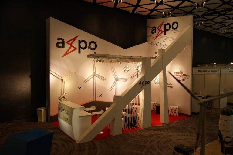Nowoczesne stoisko wystawowe Axpo ma białe ściany z logo Axpo, wzory turbin wiatrowych i wiszące światła. Aby jak wzbudzić skuteczność stoiska, obejmuje recepcję, część wypoczynkową i informacyjne wyświetlacze wewnątrz stoiska. projekt i nadzór Tatjana Kobuszewska trksystem.com