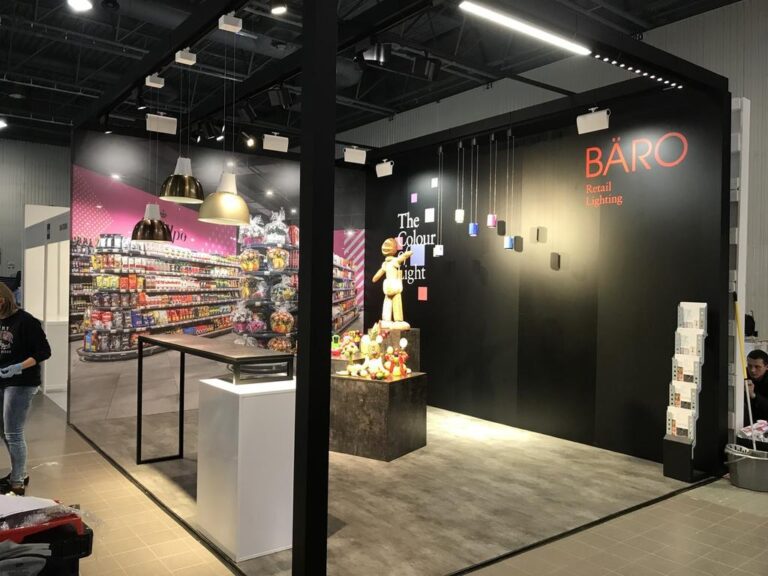 Wystawa oświetlenia detalicznego Tatjany Kobuszewskiej obejmuje nowoczesne lampy wiszące, ścianę „BARO Retail Lighting”, manekina z kolorowymi światłami, półki z przekąskami i pluszowe zabawki pod reflektorami. Projekt i nadzór trksystem.com. projekt i nadzór Tatjana Kobuszewska trksystem.com