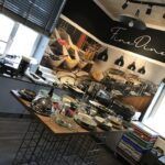 Nowoczesna jadalnia z bufetem, z przykrytymi daniami na centralnym stole. Promienie słoneczne wpadają przez żaluzje, podkreślając mural z jedzeniem podpisany „Fine Dine”. Projekt i nadzór Tatjana Kobuszewska trksystem.com. projekt i nadzór Tatjana Kobuszewska trksystem.com