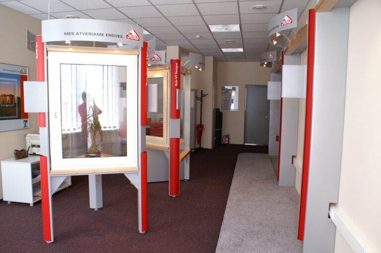 Nowoczesny salon wystawowy z szarymi i czerwonymi kabinami ekspozycyjnymi, z których każda posiada szklane gabloty. W jednej z nich znajduje się posąg postaci religijnej. Zaprojektowana przez Tatjanę Kobuszewską, z projekt i nadzór trksystem.com, przestrzeń obejmuje bordową wykładzinę i górne oświetlenie. projekt i nadzór Tatjana Kobuszewska trksystem.com