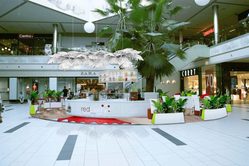 Nowoczesny Bar wyspa Redberry w Galerii Handlowej, otoczony roślinami doniczkowymi i miejscami do siedzenia, znajduje się na otwartej przestrzeni w pobliżu sklepów Zara, Centro i Curry. Obszar jest jasny, zarówno z naturalnym, jak i sztucznym światłem. projekt i nadzór Tatjana Kobuszewska trksystem.com