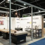 Nowoczesne stoisko wystawiennicze na targach 3Sygma Warsaw Home prezentuje armaturę kuchenną i urządzenia, w tym zlewozmywaki, baterie i kuchenki. Białe ściany eksponują logo marek takich jak Benthaüs, Armando Vicario i Asoma pośród eleganckiego oświetlenia i industrialnego wystroju. projekt i nadzór Tatjana Kobuszewska trksystem.com