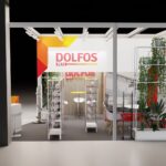 Nowoczesne stoisko targowe dla DOLFOS PETS z odważnym czerwonym, pomarańczowym i żółtym brandingiem. Stoisko ma półki na produkty, okrągły stół z krzesłami, wiszące światła, wysokie zielone rośliny i białą otwartą ramę na ciemnej podłodze. projekt i nadzór Tatjana Kobuszewska trksystem.com