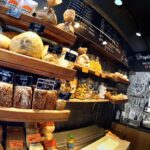 Półki w Przystanku Piekarnia eksponują różne chleby, bułki i wypieki. Każdy produkt oznaczony jest czarną metką z ceną i białym napisem. Fotoreportaż Tatjany Kobuszewskiej oddaje przytulną, rustykalną przestrzeń z polskim menu i ekspresami do kawy. projekt i nadzór Tatjana Kobuszewska trksystem.com