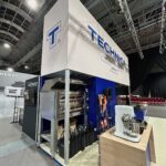 Stoisko targowe Grupy TECHNICA obejmuje duży piec, blachy do pieczenia, mikser ekspozycyjny i manekina w pomarańczowej odzieży roboczej. Wyraźny znak TECHNICA na stoisku wyróżnia się w przestronnej przemysłowej hali wystawienniczej. projekt i nadzór Tatjana Kobuszewska trksystem.com