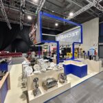 Stoisko targowe Technica Group prezentuje sprzęt gastronomiczny - naczynia, talerze, dzbanki na kawę - na białych ladach. Niebieskie ramy podtrzymują odważny napis "TECHNICA", a czerwone krzesła i reflektory podkreślają żywą atmosferę wydarzenia. projekt i nadzór Tatjana Kobuszewska trksystem.com