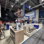 Stoisko targowe prezentuje produkty Technica Group, w tym przemysłowe urządzenia i przybory kuchenne. Jasne oświetlenie, eleganckie blaty, metalowe stojaki i nowoczesny baner tworzą czystą i zachęcającą atmosferę. projekt i nadzór Tatjana Kobuszewska trksystem.com