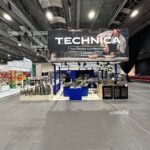 Stoisko targowe Grupy TECHNICA prezentuje profesjonalny sprzęt kuchenny na niebiesko-białych stojakach. Nad głowami duży baner przedstawia kucharzy przy pracy z hasłem "To tworzy profesjonalną kuchnię". Pozostałe stoiska widoczne są po lewej stronie. projekt i nadzór Tatjana Kobuszewska trksystem.com