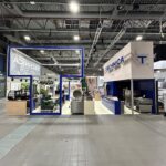 W przestronnej hali wystawienniczej z industrialnym sufitem znajduje się duże stoisko targowe Technica Group prezentujące komercyjny sprzęt kuchenny. Urządzenia, piece i maszyny są widoczne wewnątrz stoiska. W pobliżu znajdują się inne stoiska firmowe i urządzenia kuchenne. projekt i nadzór Tatjana Kobuszewska trksystem.com