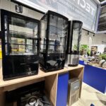 Trzy czarne lodówki nablatowe Technica Group ustawione są na drewnianej półce. Pod nimi znajduje się pojedynczy palnik gazowy. Tło przedstawia tętniące życiem stoisko targowe z różnymi stoiskami, jasnymi światłami i widocznym oznakowaniem. projekt i nadzór Tatjana Kobuszewska trksystem.com