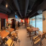 Panoramiczny widok na nowoczesną japońską restaurację Halo Mian z czerwono-szarymi ścianami, drewnianymi stołami i krzesłami, tradycyjną sztuką, zwojami kaligrafii i dużymi oknami ukazującymi zaśnieżoną ulicę na zewnątrz - spokojna scena w tej restauracji fusion chińska. projekt i nadzór Tatjana Kobuszewska trksystem.com