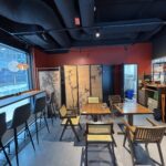 Przytulna kawiarnia Halo Mian łączy w sobie urok restauracji chińskiej z drewnianymi krzesłami i stołami, wysoką ladą barową z szarymi stołkami, bambusową sztuką na składanym ekranie, czerwono-czarnymi ścianami, odsłoniętymi kanałami wentylacyjnymi nad głową i światłem słonecznym wpadającym przez duże okna. projekt i nadzór Tatjana Kobuszewska trksystem.com