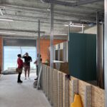 Trzy osoby stoją rozmawiając wewnątrz częściowo zbudowanego pomieszczenia z odsłoniętymi metalowymi ramami i niedokończonymi ścianami, prawdopodobnie przyszłej restauracji Halo Mian. Otaczają ich materiały budowlane, a naturalne światło wpada przez duże okna po lewej stronie. projekt i nadzór Tatjana Kobuszewska trksystem.com