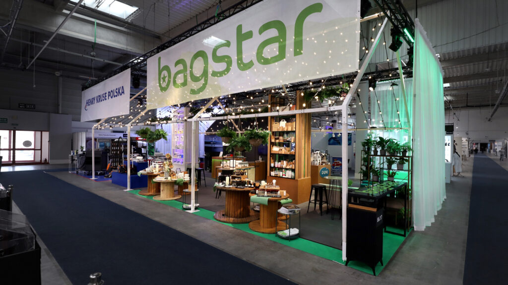 Stoisko targowe Bagstar z dużym białym szyldem, lampkami sznurkowymi, zielono-białym wystrojem i ekspozycją różnych produktów na drewnianych stołach - idealne dla osób zainteresowanych stoiskiem targowym w pytaniach i odpowiedziach. Zieleń dodatkowo zachęca do odwiedzin. Targi EuroGastro, Ptak Warsaw Expo.projekt i nadzór Tatjana Kobuszewska trksystem.com