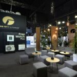 Nowoczesne stoisko wystawiennicze Gree na Ptak Warsaw Expo obejmuje klimatyzatory na wystawie, czarną ścianę z białym tekstem oraz część wypoczynkową z szarymi sześcianowymi krzesłami i zielenią, a wszystko to oświetlone przez wiszące okrągłe światła - idealne dla Międzynarodowych Targów HVAC. projekt i nadzór Tatjana Kobuszewska trksystem.com