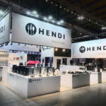 Dobrze oświetlone stoisko wystawowe firmy HENDI, na którym na białych blatach znajdują się naczynia i urządzenia kuchenne. Duże banery wyświetlają logo HENDI i "Narzędzia dla szefów kuchni". Obszar pytań i odpowiedzi wita odwiedzających w tej przestronnej, nowoczesnej przestrzeni centrum kongresowego. projekt i nadzór Tatjana Kobuszewska trksystem.com