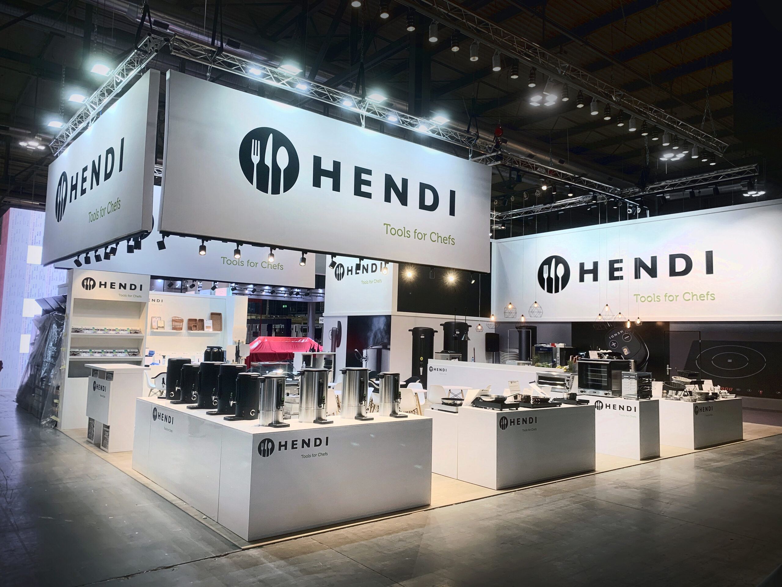 Dobrze oświetlone stoisko wystawowe firmy HENDI, na którym na białych blatach znajdują się naczynia i urządzenia kuchenne. Duże banery wyświetlają logo HENDI i "Narzędzia dla szefów kuchni". Obszar pytań i odpowiedzi wita odwiedzających w tej przestronnej, nowoczesnej przestrzeni centrum kongresowego. projekt i nadzór Tatjana Kobuszewska trksystem.com