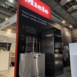Stoisko targowe z dużym czerwono-czarnym napisem Miele nad ekspozycją zmywarek przemysłowych. Polski tekst wyjaśnia rozwiązania 360PRO. Stoisko znajduje się w oświetlonej hali wystawowej z widocznymi rurami sufitowymi i stojakami w pobliżu. projekt i nadzór Tatjana Kobuszewska trksystem.com