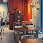 Przytulne wnętrze restauracji-halomian-detal-czerwony z drewnianymi stołami i krzesłami, ścianą z czerwonej cegły, wiszącymi lampionami, zwojami i kompozycjami kwiatowymi. Czarna szafa, wieszaki na płaszcze i delikatne oświetlenie dopełniają ciepłą, zachęcającą atmosferę. projekt i nadzór Tatjana Kobuszewska trksystem.com