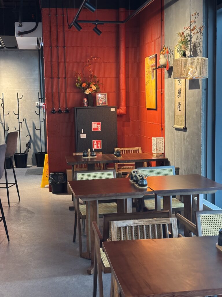 Przytulne wnętrze restauracji-halomian-detal-czerwony z drewnianymi stołami i krzesłami, ścianą z czerwonej cegły, wiszącymi lampionami, zwojami i kompozycjami kwiatowymi. Czarna szafa, wieszaki na płaszcze i delikatne oświetlenie dopełniają ciepłą, zachęcającą atmosferę. projekt i nadzór Tatjana Kobuszewska trksystem.com