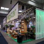 Nowoczesne stoisko targowe Stoisko Bagstar i Henry Kruse na Eurogastro 2026 w Ptak Warsaw Expo zawiera drewniane akcenty, sznurki świetlne, zieleń i starannie ułożone produkty w przestronnej, industrialnej hali wystawienniczej. projekt i nadzór Tatjana Kobuszewska trksystem.com