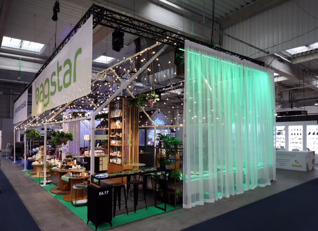 Nowoczesne stoisko targowe Stoisko Bagstar i Henry Kruse na Eurogastro 2026 w Ptak Warsaw Expo zawiera drewniane akcenty, sznurki świetlne, zieleń i starannie ułożone produkty w przestronnej, industrialnej hali wystawienniczej. projekt i nadzór Tatjana Kobuszewska trksystem.com