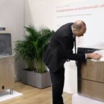 W stoisku Smeg Professional - 50 m² w sąsiedztwie Grafeny, mężczyzna w garniturze poleruje zmywarkę ze stali nierdzewnej na wystawie, a obok znajduje się inna zmywarka, butelka z rozpylaczem, rośliny doniczkowe i polskie plakaty informacyjne. projekt i nadzór Tatjana Kobuszewska trksystem.com